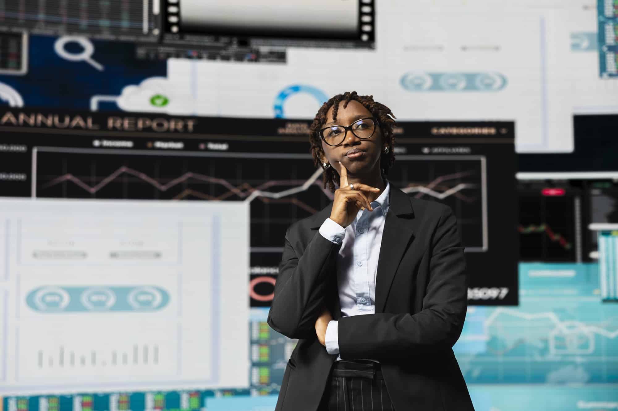 An African female business leader looking thoughtfully at digital financial dashboards and performance analytics screens.